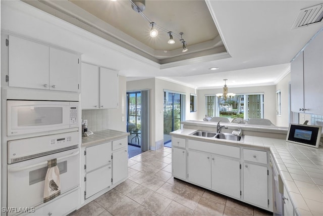 kitchen featuring white appliances, tile countertops, a raised ceiling, and sink