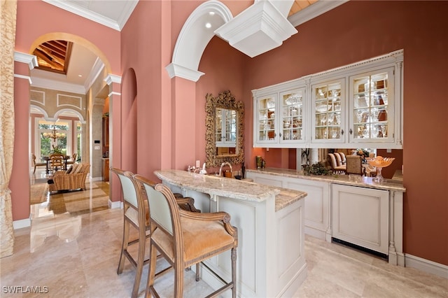 bar with ornate columns, white cabinetry, crown molding, a towering ceiling, and light stone countertops