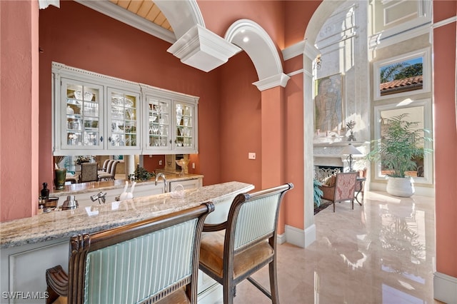 bar with white cabinetry, a fireplace, light stone countertops, and decorative columns