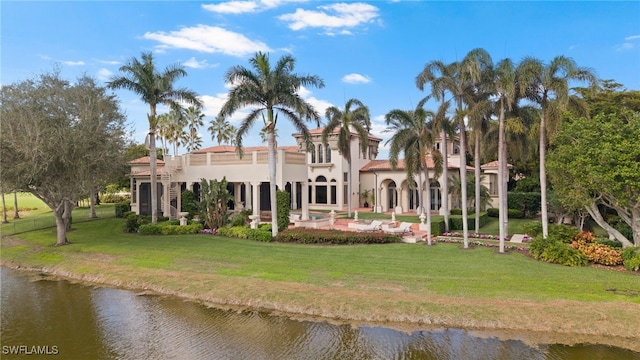 back of property with a water view, a patio area, and a lawn