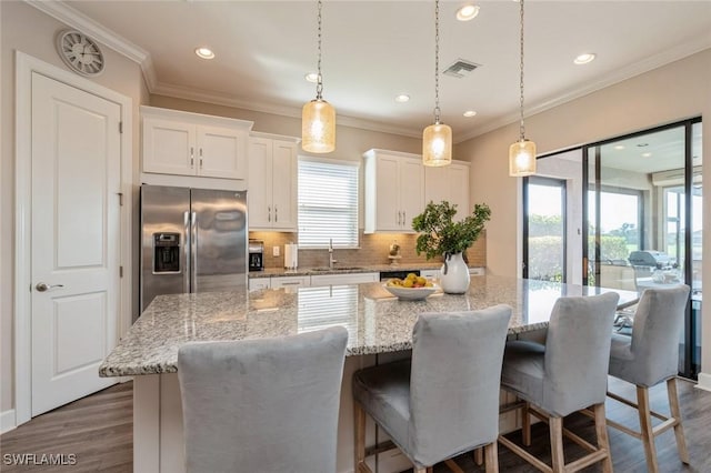 kitchen with decorative light fixtures, stainless steel fridge, a center island, and white cabinets