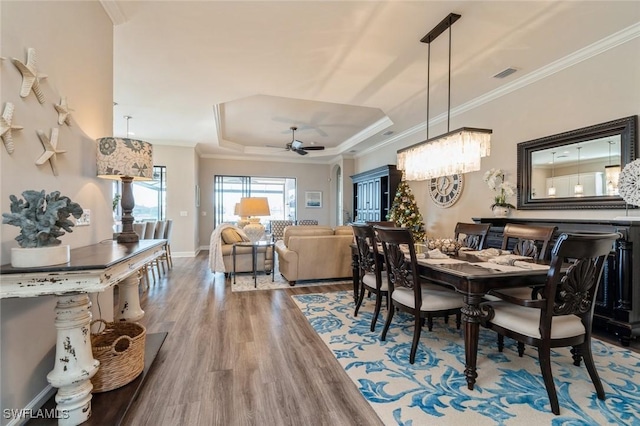 dining room featuring hardwood / wood-style flooring, ornamental molding, a raised ceiling, and ceiling fan with notable chandelier