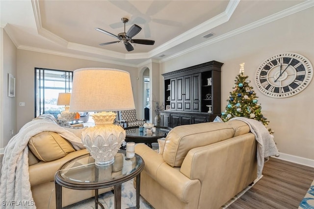 living room with ceiling fan, ornamental molding, dark hardwood / wood-style flooring, and a raised ceiling