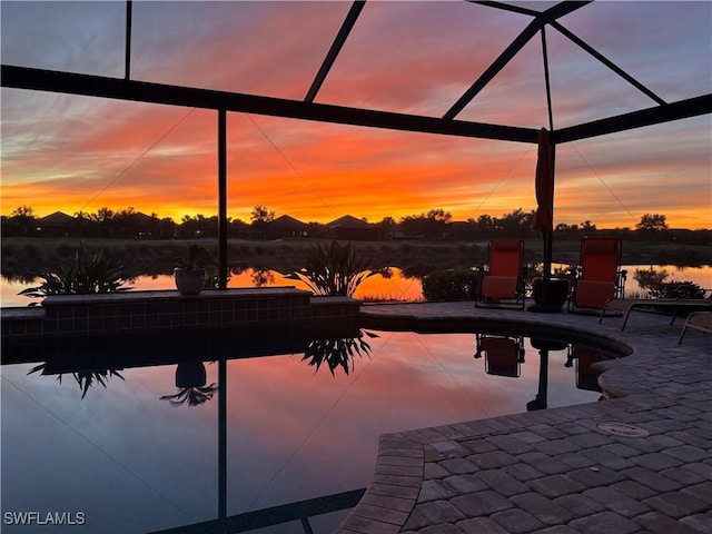 pool at dusk with a water view, glass enclosure, and a patio area