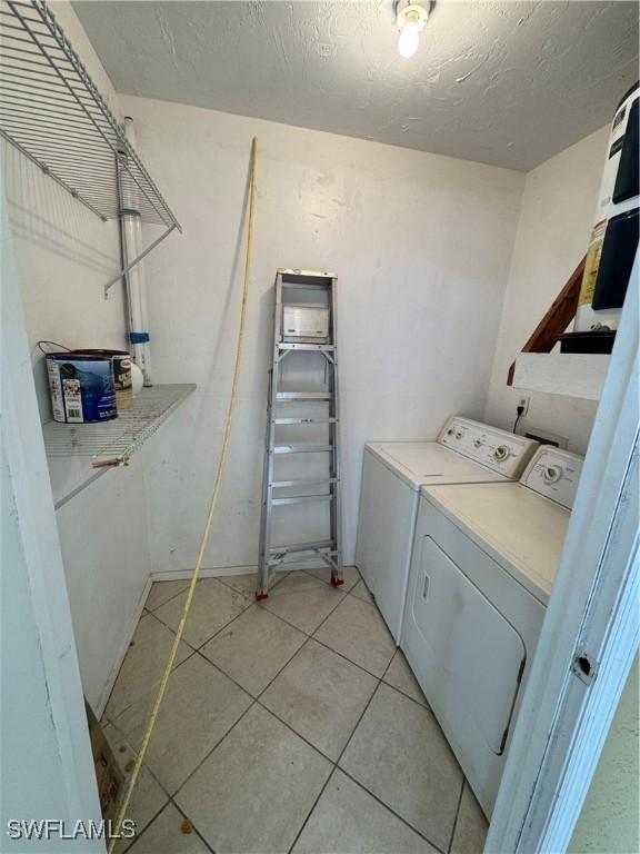 laundry room featuring light tile patterned floors, a textured ceiling, and washer and clothes dryer