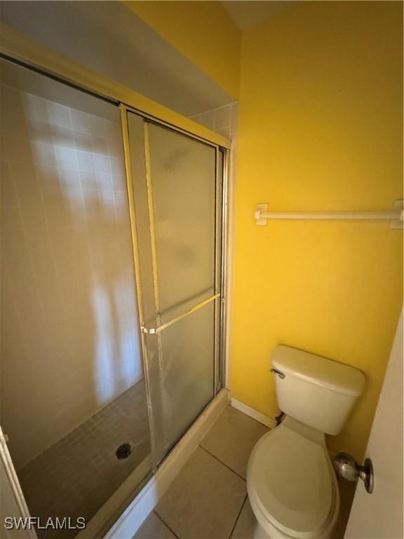 bathroom with tile patterned floors, a shower with shower door, and toilet