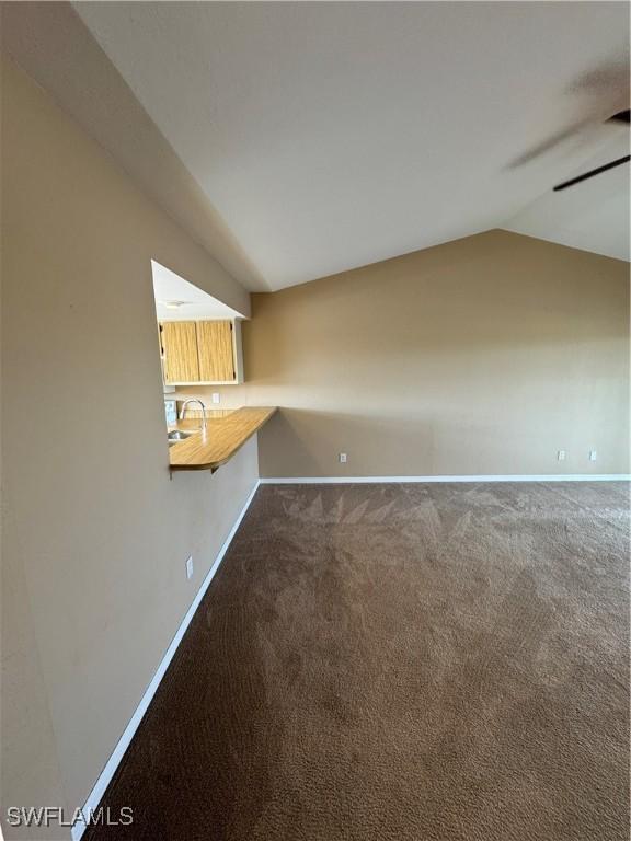 unfurnished living room featuring carpet floors, vaulted ceiling, ceiling fan, and sink