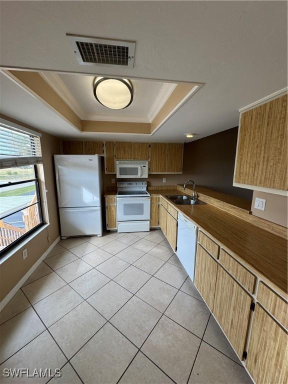 kitchen with a raised ceiling, white appliances, sink, and light tile patterned floors