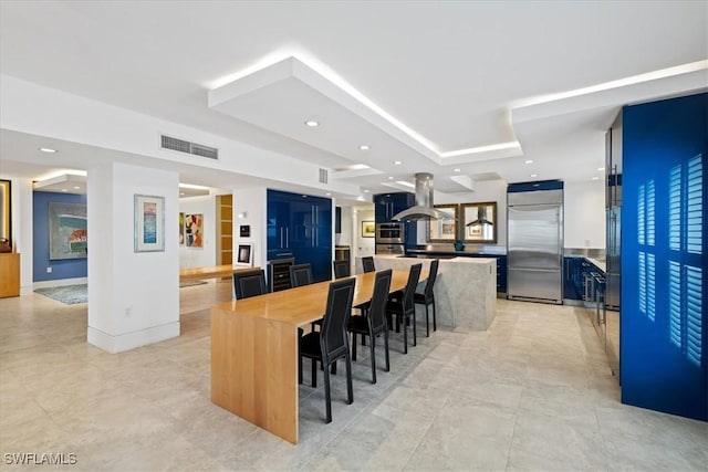 kitchen featuring butcher block countertops, a breakfast bar area, built in refrigerator, a center island, and island range hood