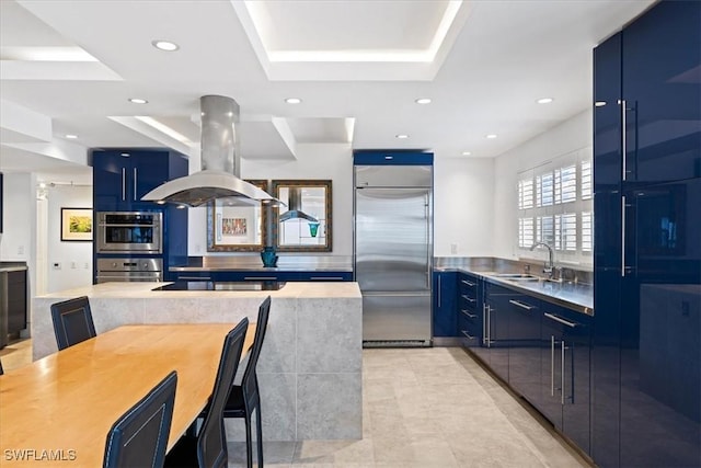 kitchen with built in refrigerator, island exhaust hood, sink, and blue cabinetry