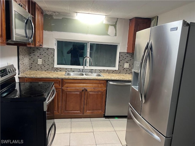 kitchen featuring light stone countertops, backsplash, stainless steel appliances, sink, and light tile patterned floors