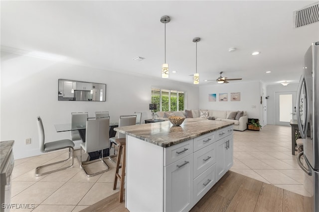 kitchen featuring dark stone counters, light tile patterned floors, a kitchen island, white cabinetry, and stainless steel refrigerator