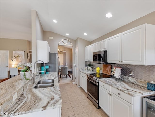 kitchen featuring lofted ceiling, white cabinetry, stainless steel appliances, sink, and light stone counters