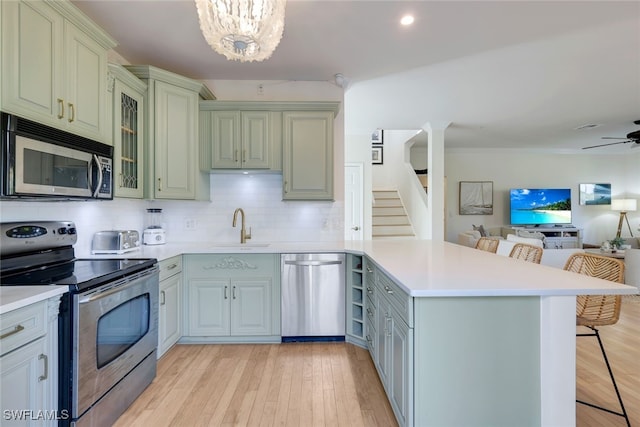 kitchen with a breakfast bar, sink, appliances with stainless steel finishes, tasteful backsplash, and kitchen peninsula