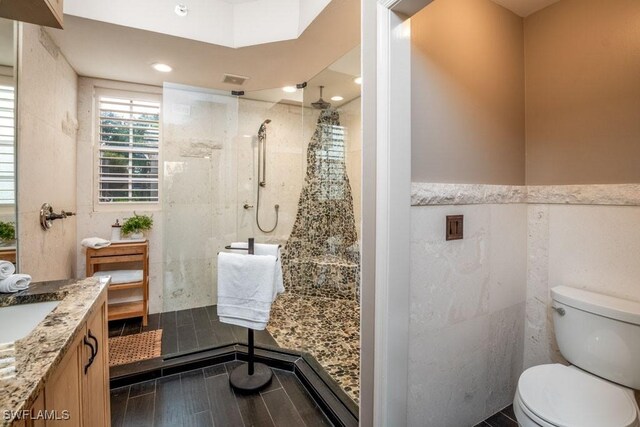 bathroom featuring tiled shower, vanity, tile walls, and toilet