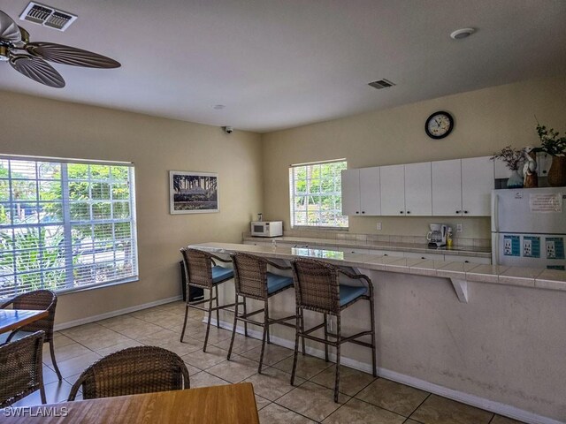 kitchen with white appliances, white cabinets, ceiling fan, a wealth of natural light, and a kitchen bar