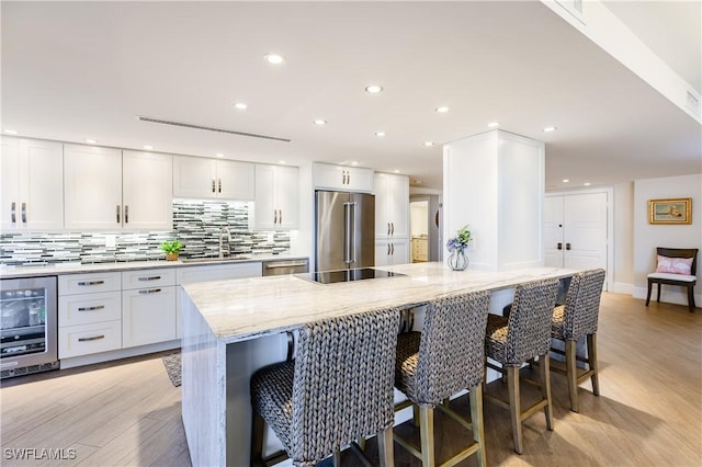 kitchen with light stone countertops, a kitchen bar, white cabinetry, stainless steel appliances, and beverage cooler