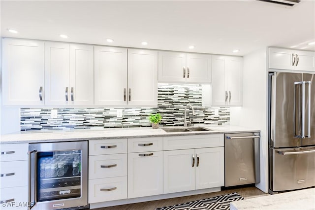 kitchen with backsplash, white cabinets, sink, appliances with stainless steel finishes, and beverage cooler