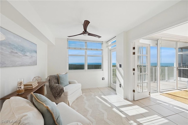 living area with light tile patterned floors, a water view, and ceiling fan