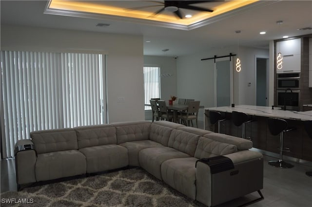 living room with ceiling fan, a barn door, a raised ceiling, and crown molding