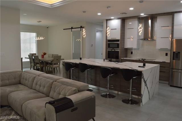 kitchen with pendant lighting, wall chimney exhaust hood, a barn door, appliances with stainless steel finishes, and a large island