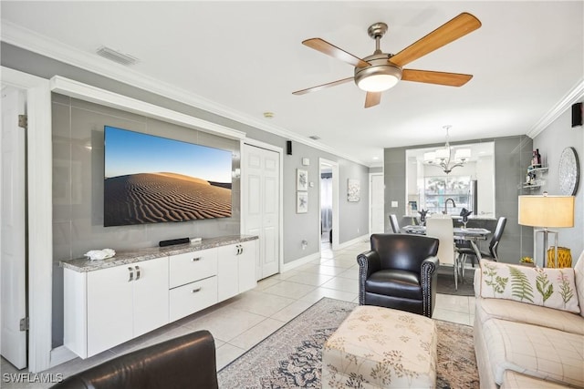 living area with light tile patterned flooring, ceiling fan with notable chandelier, visible vents, baseboards, and ornamental molding