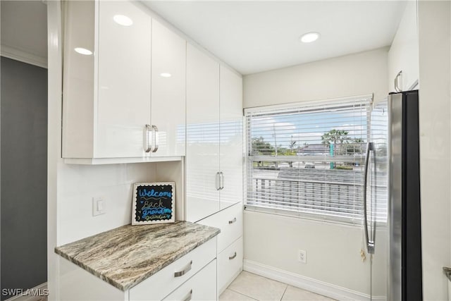 kitchen with white cabinets, light tile patterned floors, light stone counters, and stainless steel refrigerator