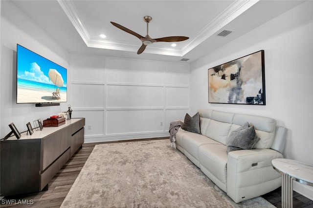 living room with light hardwood / wood-style floors, a raised ceiling, and crown molding