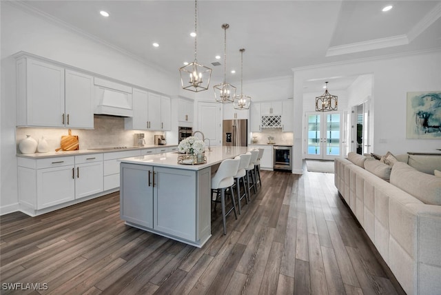 kitchen featuring tasteful backsplash, stainless steel appliances, beverage cooler, a center island with sink, and white cabinetry