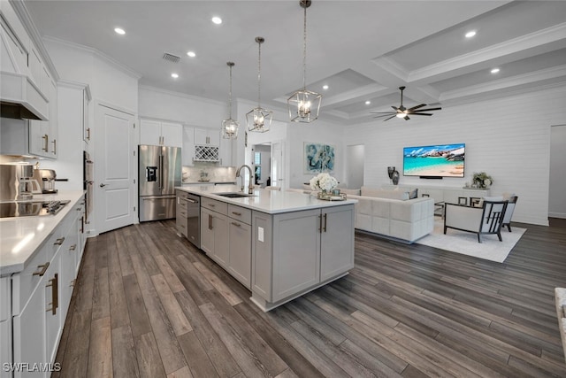 kitchen with beam ceiling, sink, stainless steel appliances, decorative light fixtures, and a center island with sink