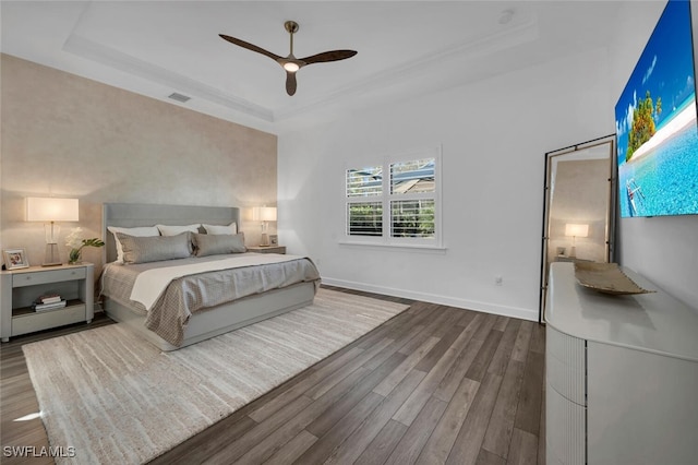 bedroom with ceiling fan, dark hardwood / wood-style flooring, and a raised ceiling