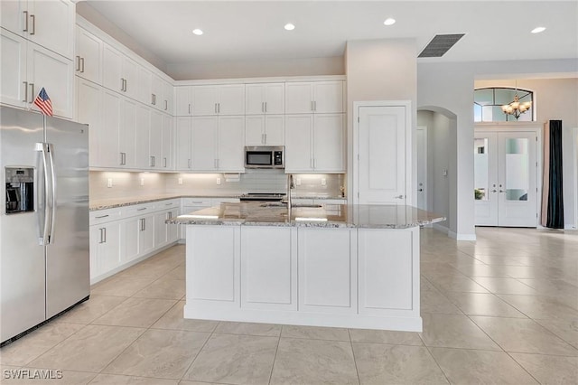 kitchen with light stone counters, stainless steel appliances, sink, a center island with sink, and white cabinetry