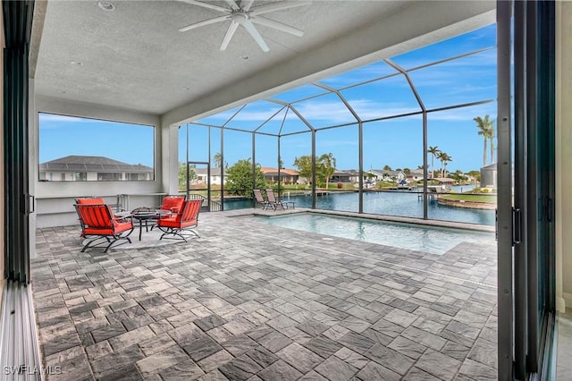 view of pool with glass enclosure, ceiling fan, a water view, and a patio