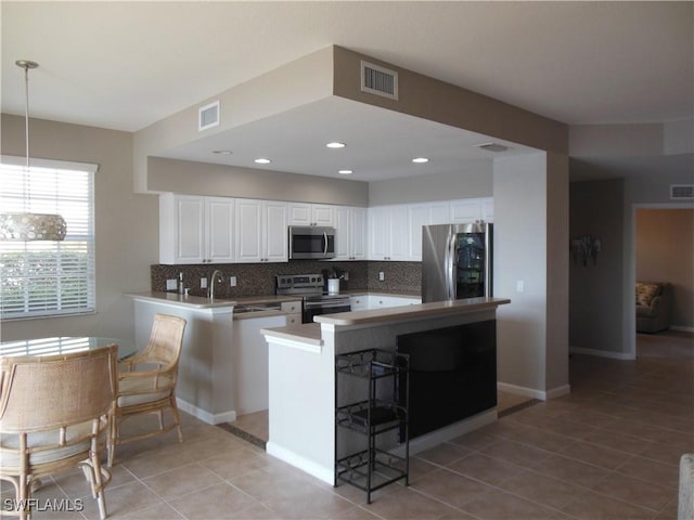 kitchen featuring white cabinetry, hanging light fixtures, kitchen peninsula, light tile patterned flooring, and appliances with stainless steel finishes