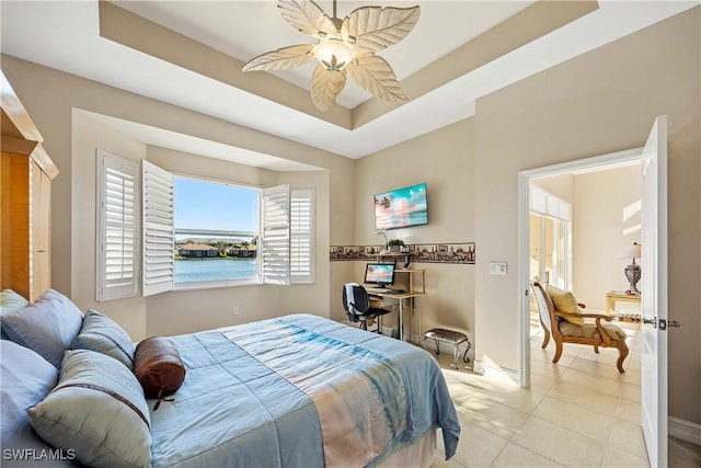 tiled bedroom with ceiling fan and a tray ceiling