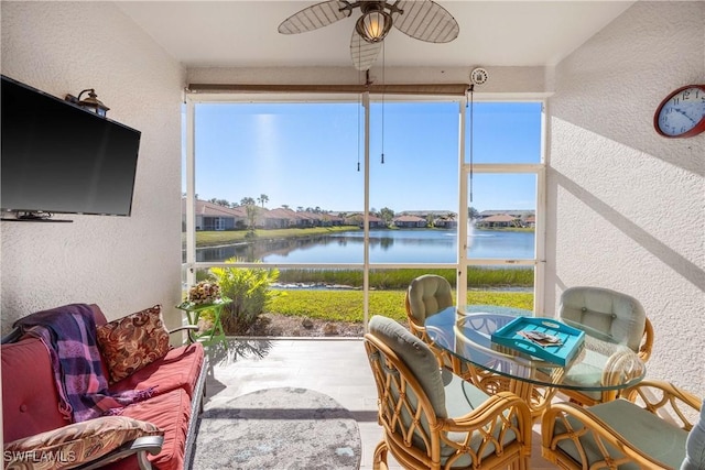 sunroom featuring ceiling fan and a water view