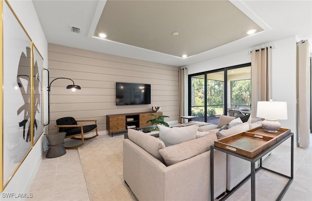 living room featuring wood walls, light tile patterned floors, and a tray ceiling