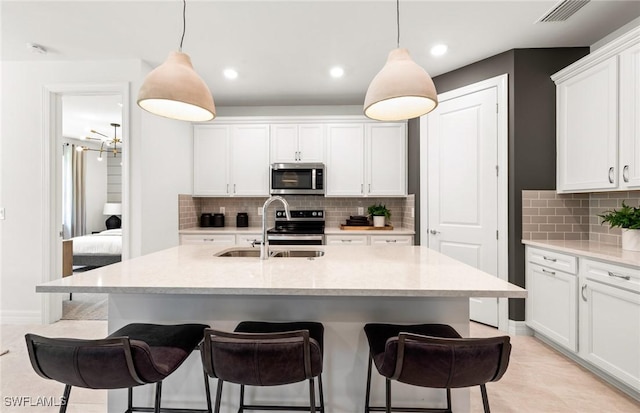 kitchen featuring decorative light fixtures, white cabinetry, stainless steel appliances, and a kitchen island with sink