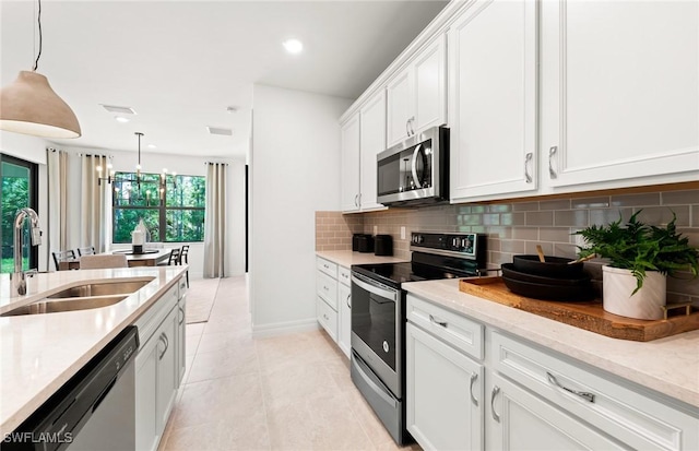 kitchen featuring stainless steel appliances, sink, light tile patterned floors, white cabinetry, and hanging light fixtures