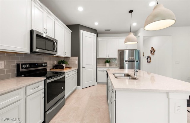 kitchen with white cabinetry, sink, hanging light fixtures, stainless steel appliances, and a kitchen island with sink