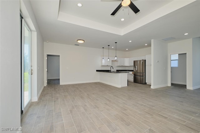 unfurnished living room with light hardwood / wood-style floors, a raised ceiling, ceiling fan, and sink