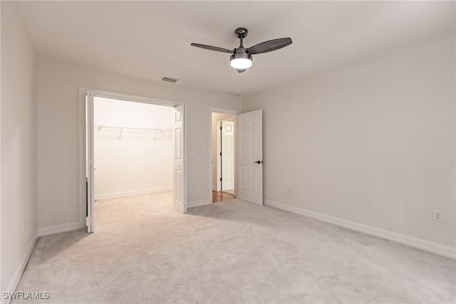 unfurnished bedroom with ceiling fan, a walk in closet, a closet, and light colored carpet