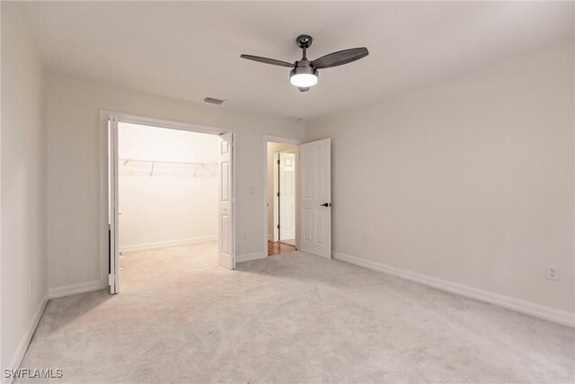 unfurnished bedroom featuring light carpet, a walk in closet, a closet, and ceiling fan