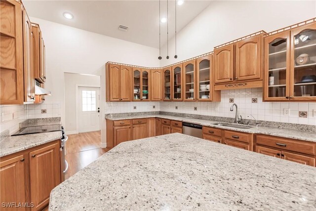 kitchen with high vaulted ceiling, sink, backsplash, stainless steel appliances, and light stone countertops