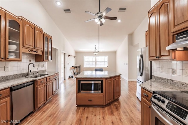 kitchen with vaulted ceiling, a kitchen island, sink, light stone countertops, and stainless steel appliances