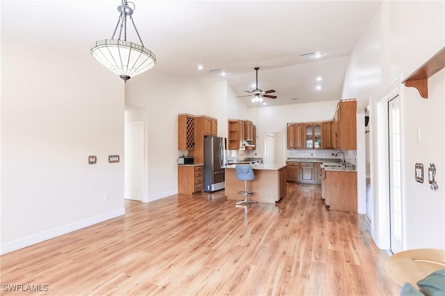 kitchen with light hardwood / wood-style floors, a kitchen island, sink, stainless steel refrigerator, and hanging light fixtures