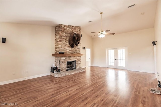 unfurnished living room with hardwood / wood-style floors, a stone fireplace, ceiling fan, french doors, and vaulted ceiling