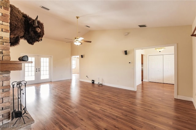 unfurnished living room featuring ceiling fan, dark hardwood / wood-style floors, a stone fireplace, high vaulted ceiling, and french doors