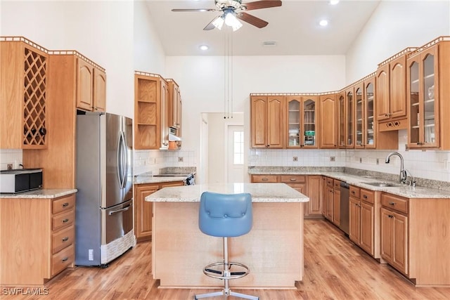 kitchen with appliances with stainless steel finishes, a towering ceiling, a kitchen island, light hardwood / wood-style flooring, and sink