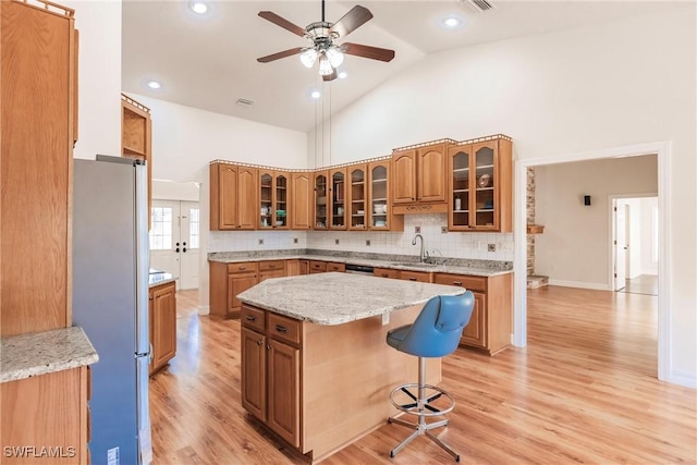 kitchen featuring a center island, sink, stainless steel fridge, high vaulted ceiling, and a breakfast bar